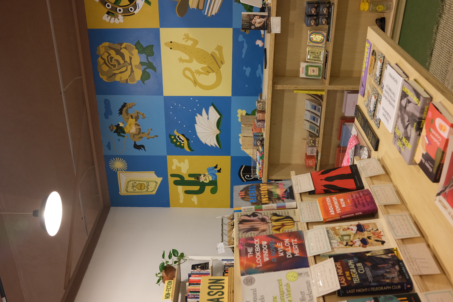 A table full of books sits in front of blue and yellow mural.
