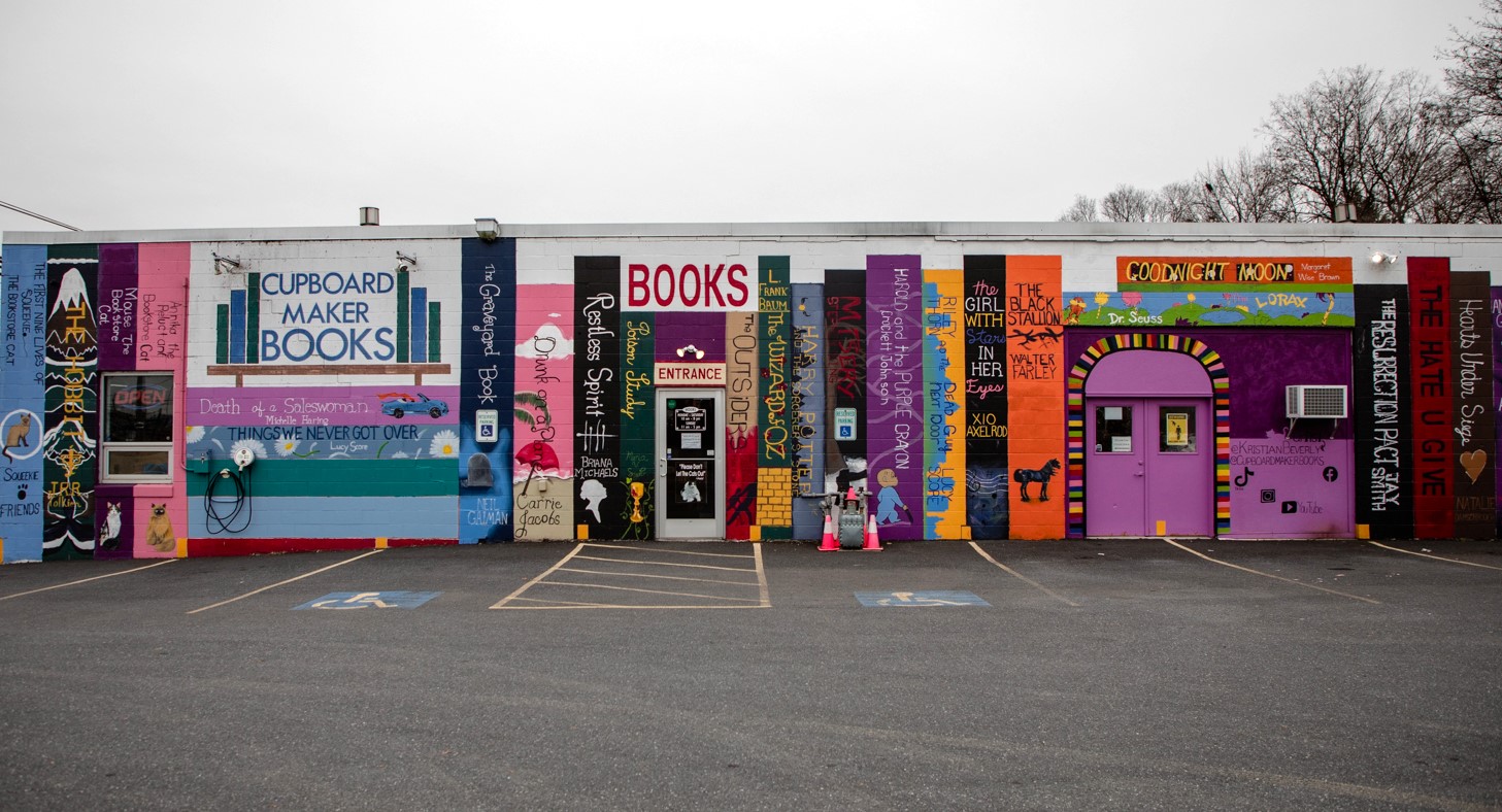 The exterior of Cupboard Maker Books. A white building with a low roof has been convered in paintings of spines of books.