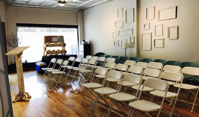 A room filled with empty white event chairs in front of a white wall