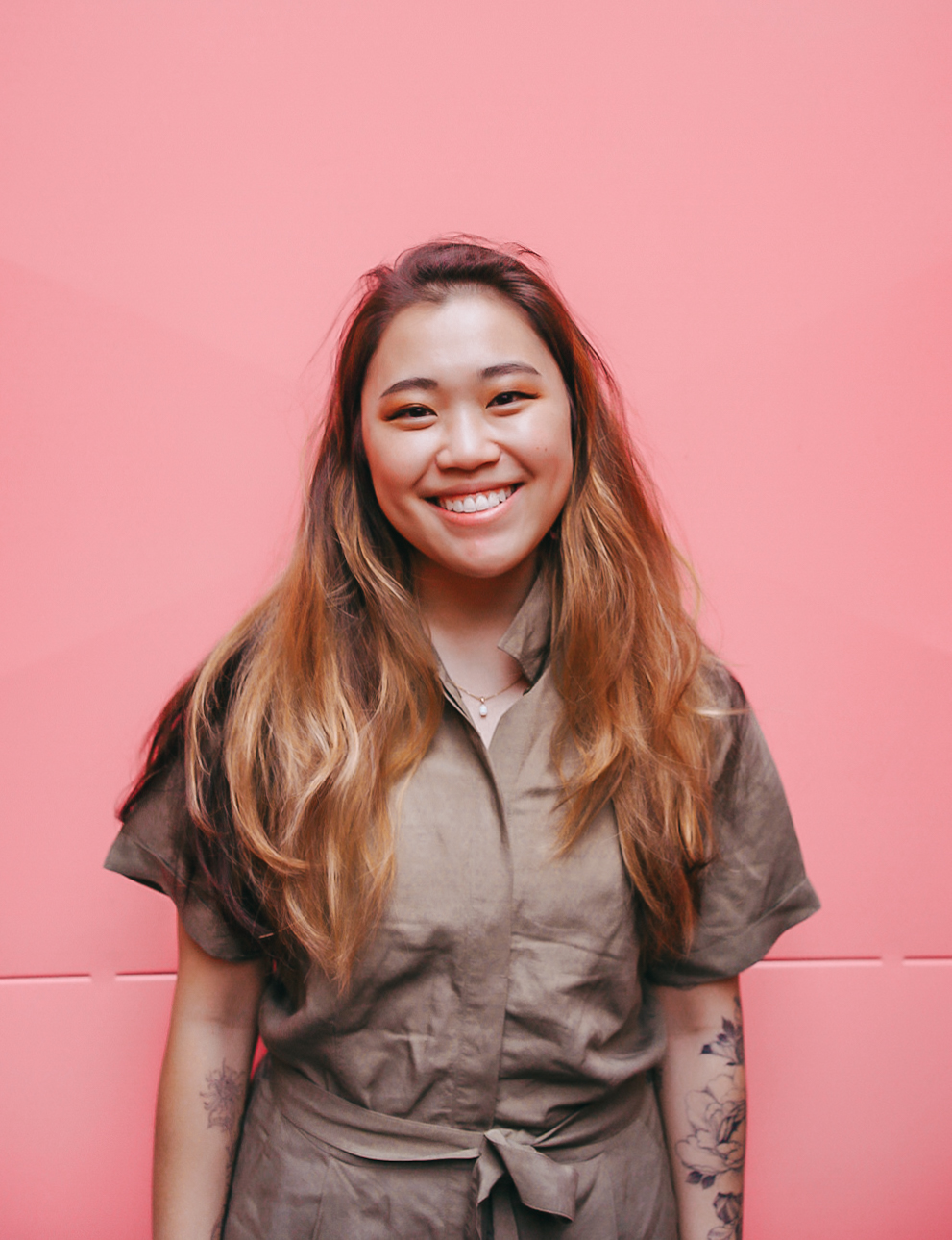 Linzi Murray, founder of Reading in Public smiles in front of a pink background.