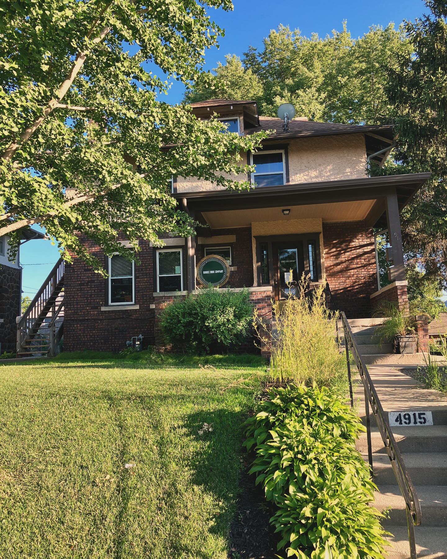 A brick house surrounded by trees. A stairway leads up to a porch with a Dundee Book Company sign.